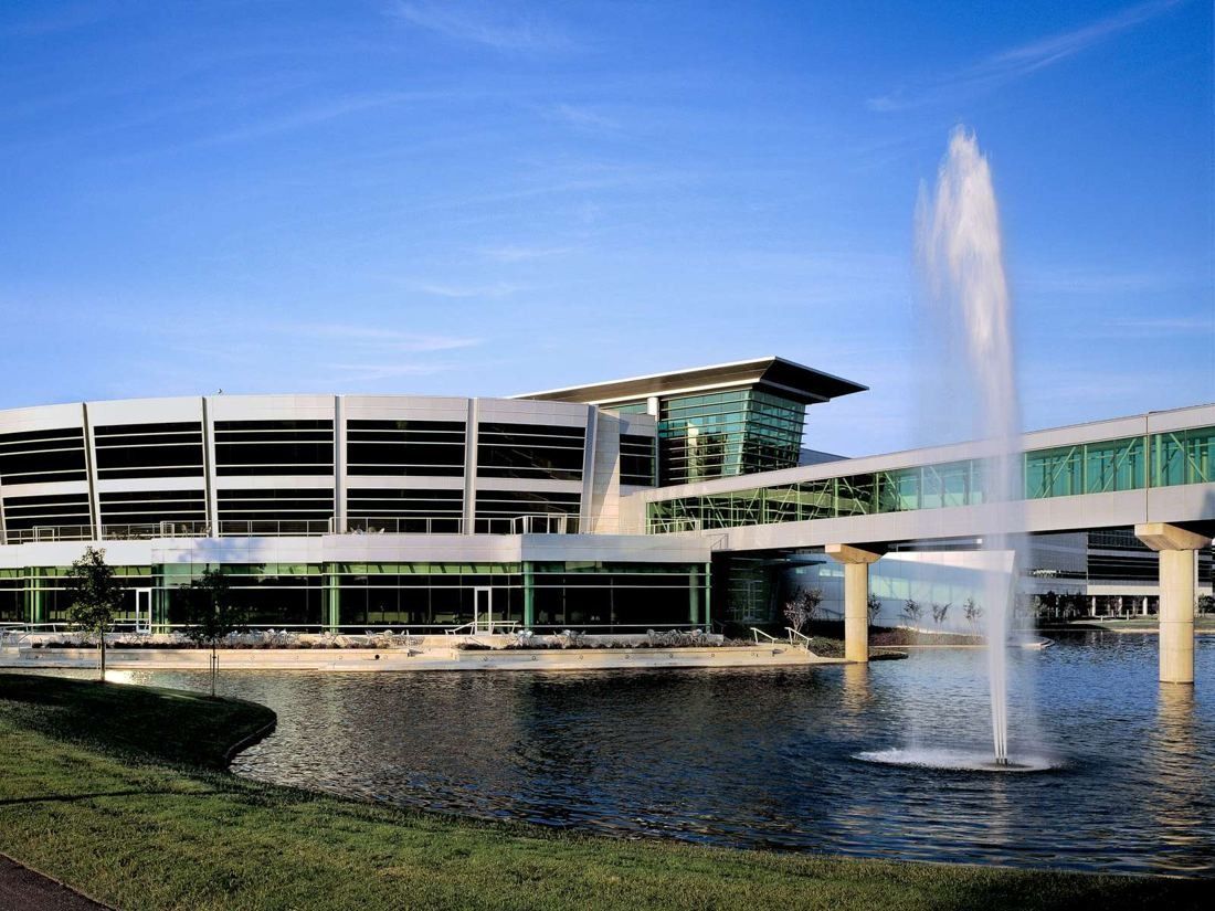 FedEx: Curved four-story building with horizontal bands, a glass skyway and a fountain in the pond in front
