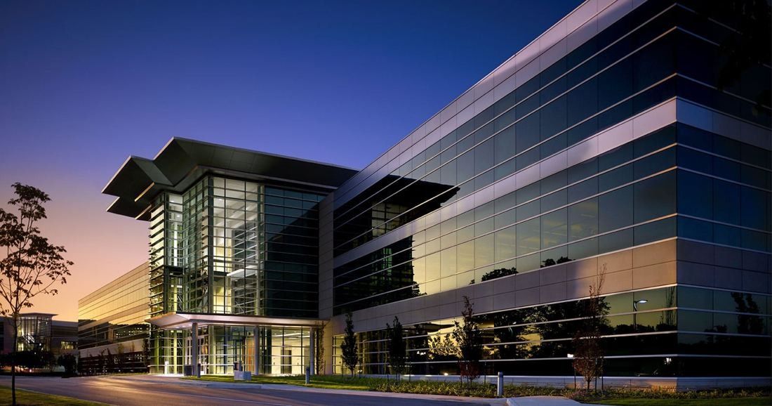 FedEx: Glass office building with a projecting flat roof at dusk, lights on inside