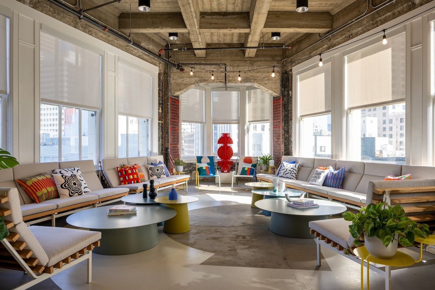 Figma: Bright lounge with long sofas, colourful cushions and coffee tables beneath tall windows