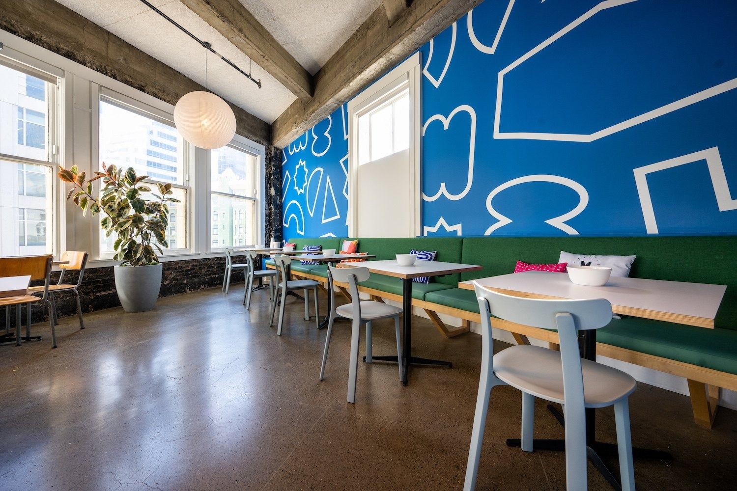 Figma: Cafe seating with green banquettes and tables beside a blue patterned wall and large windows