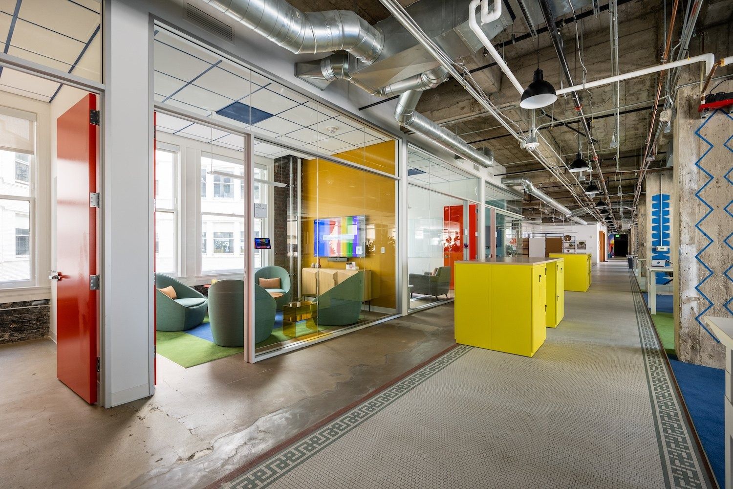 Figma: Corridor with exposed ducts past glass-walled meeting rooms in bright colours