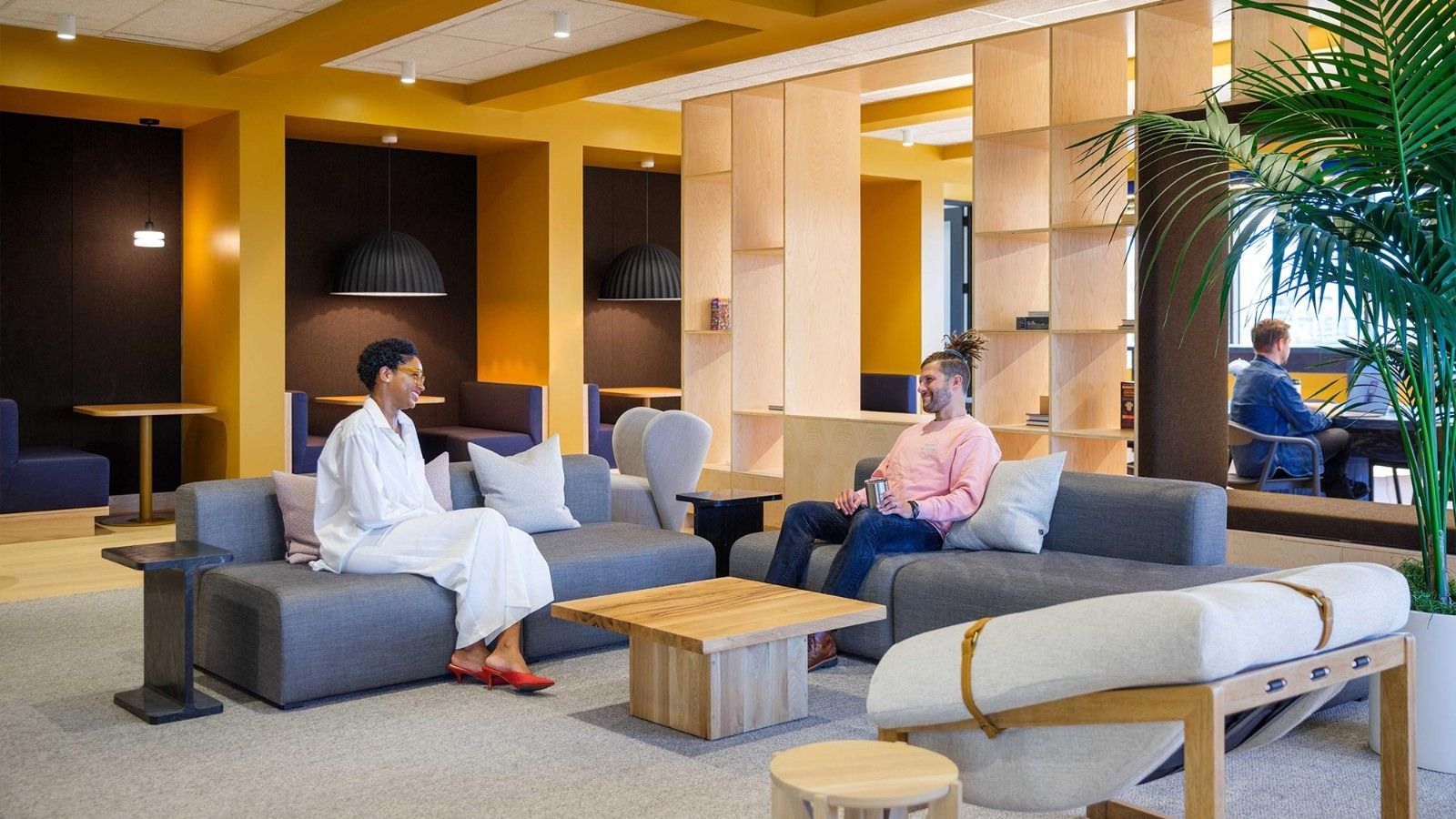 A lounge with grey sofas and wooden shelves under a yellow ceiling and plants