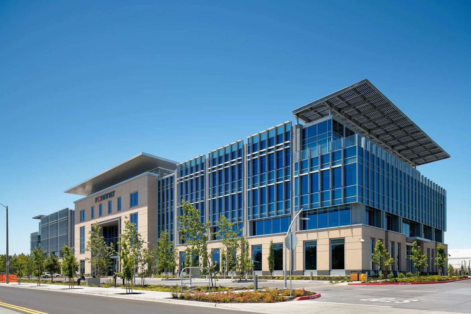 Four-story glass and stone office building with a wide flat solar canopy on the roof, under a clear blue sky