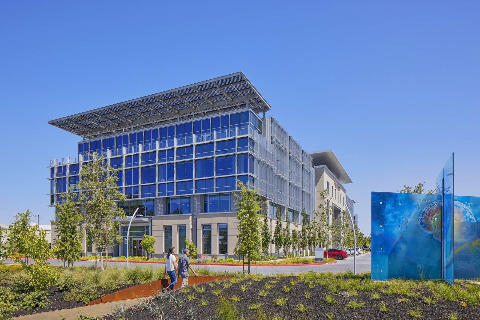 Fortinet: Glass office wing behind a planted landscape with a large blue sculpture panel at right