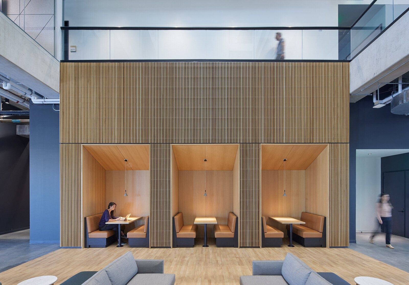 Fortinet: Three wood-lined booths with tan bench seating set into a tall slatted wood wall, facing grey sofas