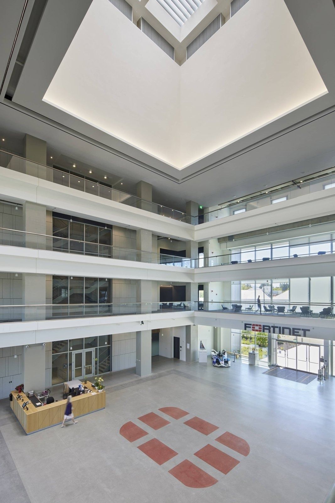 Fortinet: View up a tall white atrium with balconies on several levels and a skylight, with a red logo pattern on the floor