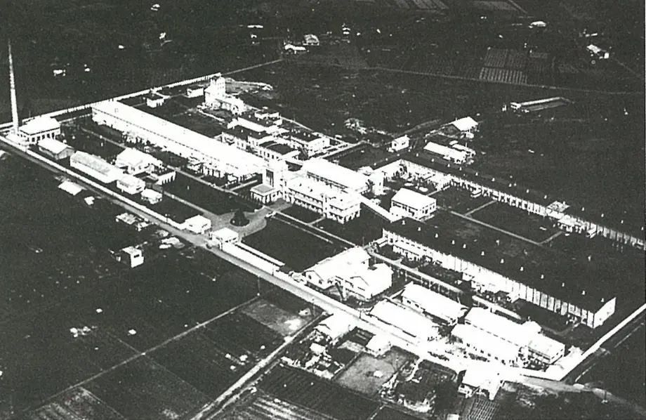 Black-and-white aerial photo of low factory buildings among fields