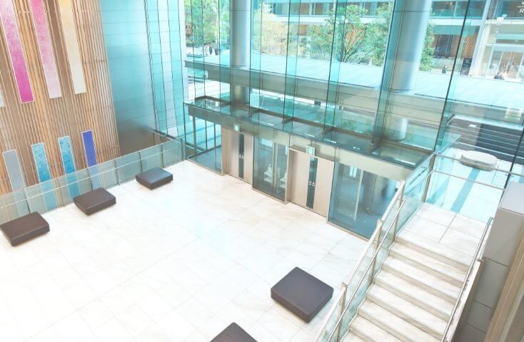 Fujifilm: Double-height lobby with glass balustrades, a staircase and square seats on a white floor