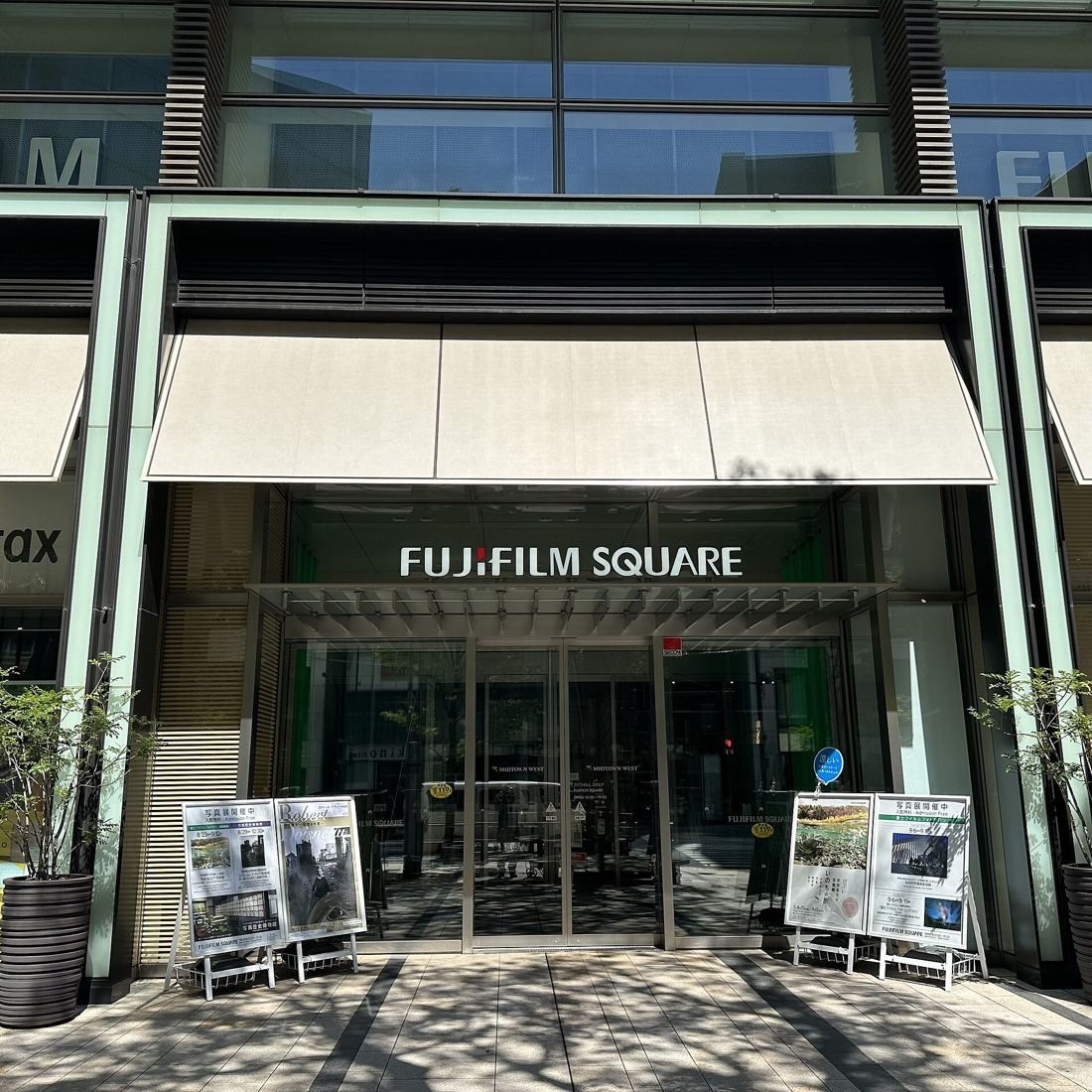 Fujifilm: Glass entrance doors under a canopy with the Fujifilm Square sign, exhibition boards on either side