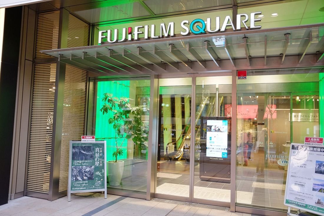 Fujifilm: Glass entrance with the Fujifilm Square sign, green-lit interior and exhibition posters