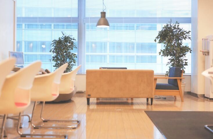 Fujifilm: Lounge with white chairs, a sofa and potted plants by tall windows