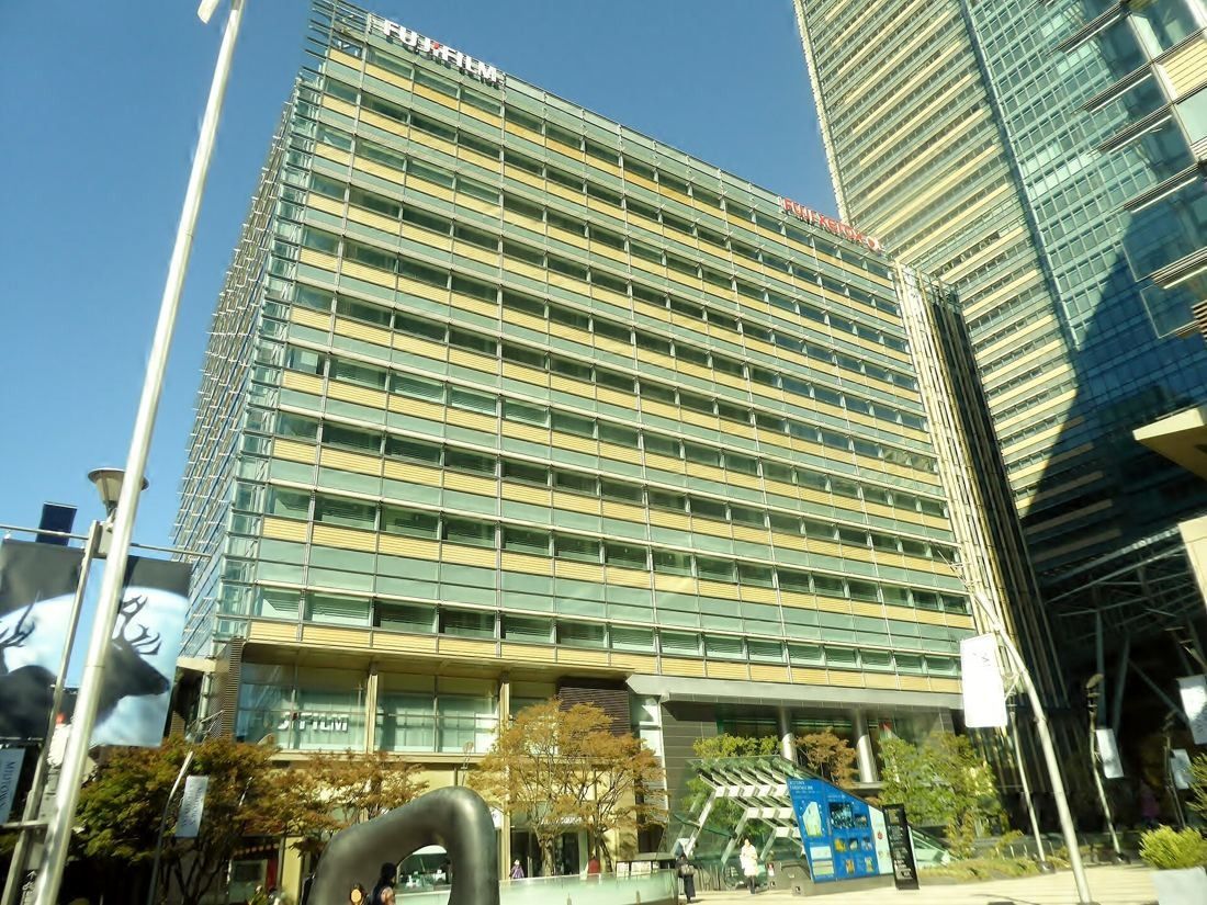 Fujifilm: Office building with layered glass and metal facade seen from a plaza with a sculpture in front