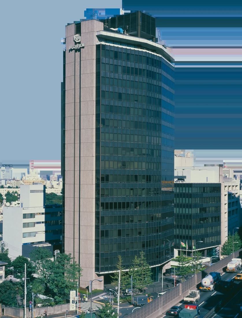 Tall slender office tower rising above a street with trees