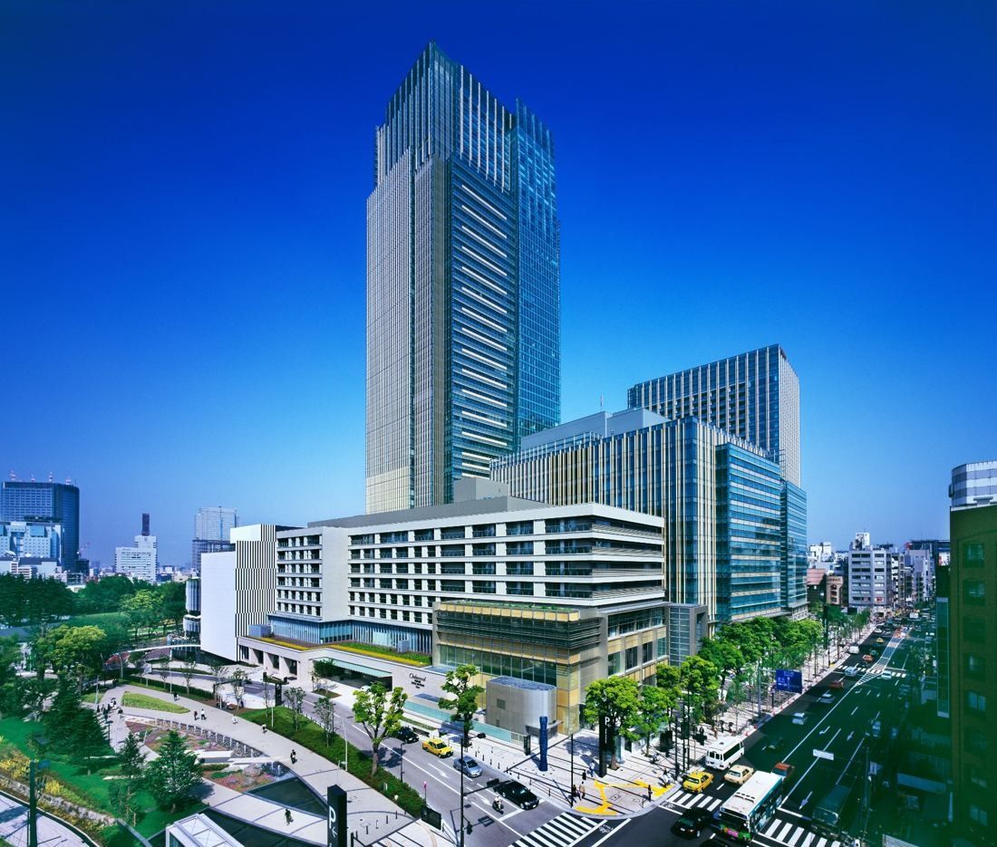 Fujifilm: Tall tower with lower buildings at its base beside a tree-lined avenue