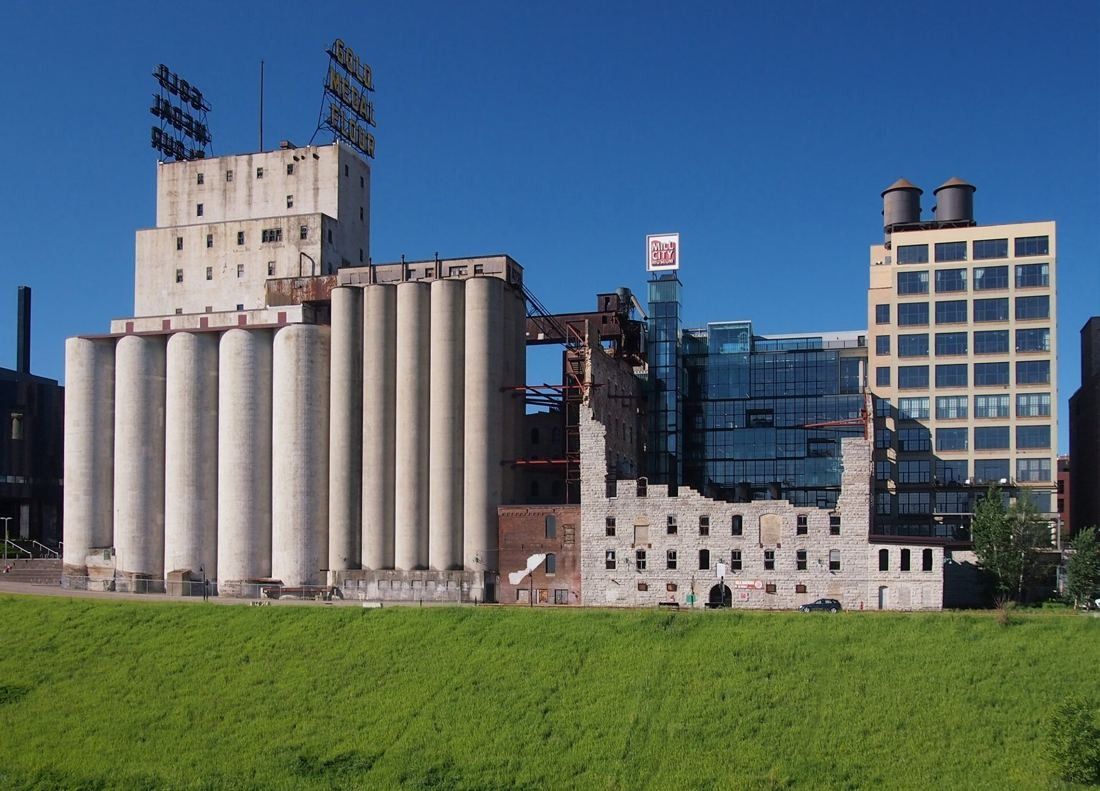 Concrete grain silos and the ruined stone walls of a mill beside newer glass buildings