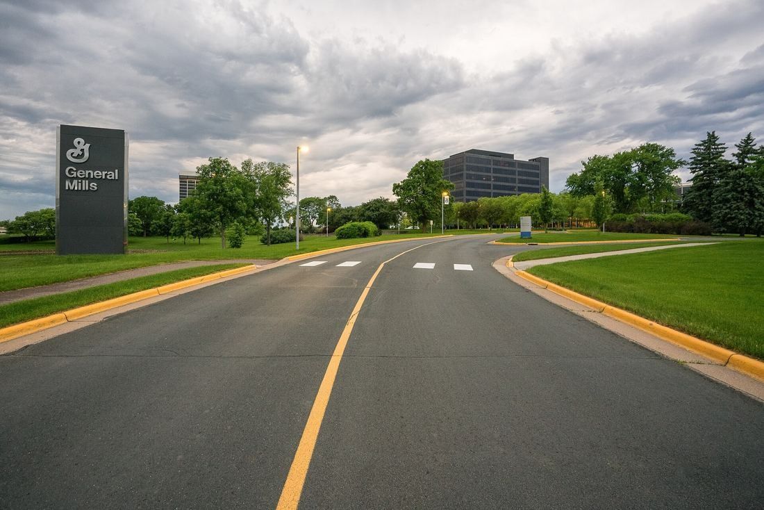 General Mills: Curving entrance road through lawns toward a low office building, with a sign at the roadside
