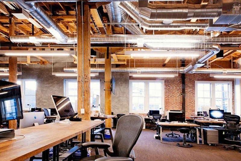 Open office with timber columns, brick walls and long wooden desks