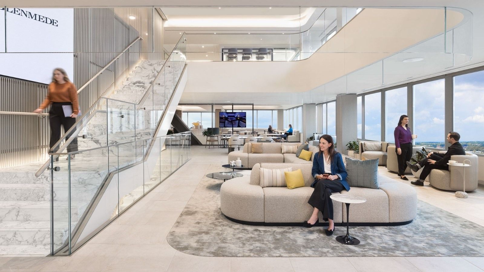 A bright atrium with a glass stair and curved sofas