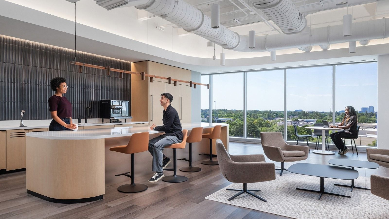 Group 1 Automotive: A café counter with orange stools and lounge chairs by a wall of windows