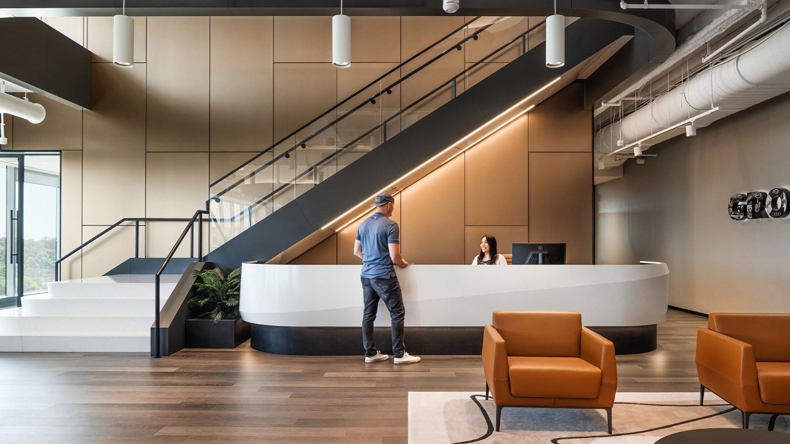 A curved white reception desk with orange armchairs below a black stair