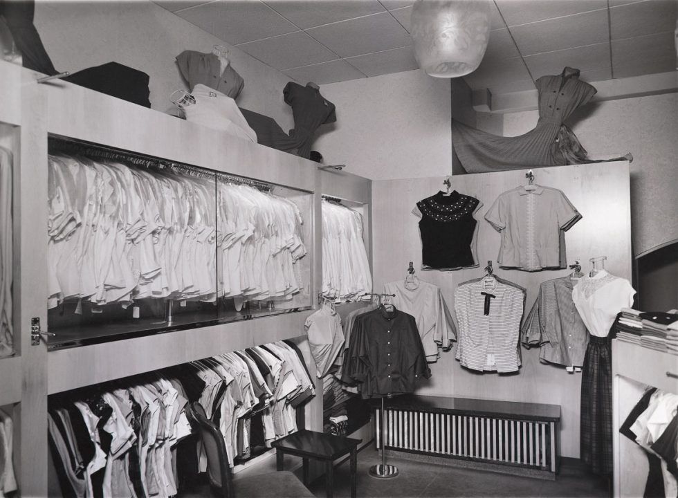 Black-and-white photo of shirts and blouses on display in a small shop