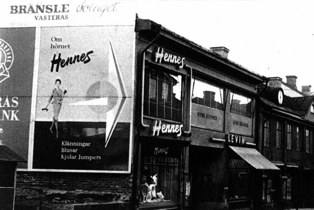 Black-and-white street view of an early Hennes store front