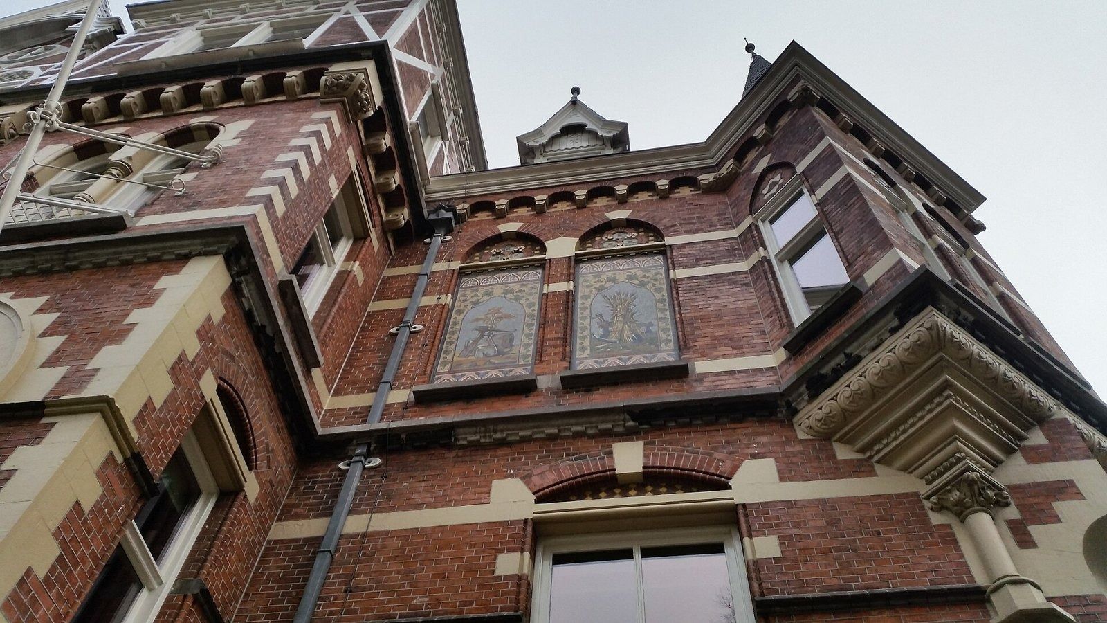 Heineken: Red-and-cream brick villa facade with a bay window and tiled panels, seen from below