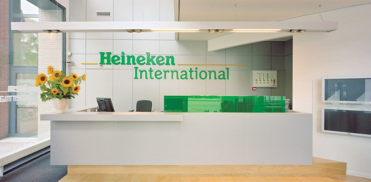Heineken: White reception desk with green lettering on the wall behind and a vase of sunflowers