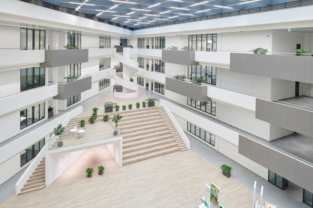 Henkel: Bright multi-storey atrium under a glass roof with a wide central staircase and planted balconies