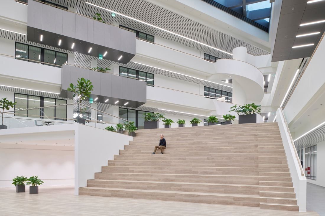 Henkel: Broad wooden staircase rising through a white atrium with plants