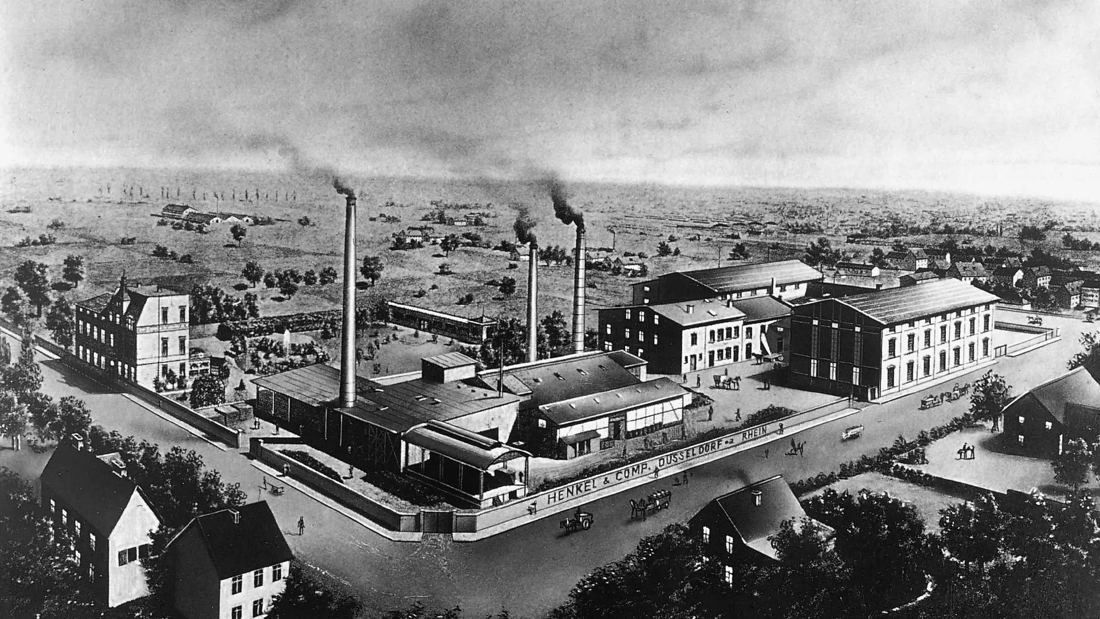 Old photograph of a factory complex with chimneys on open land