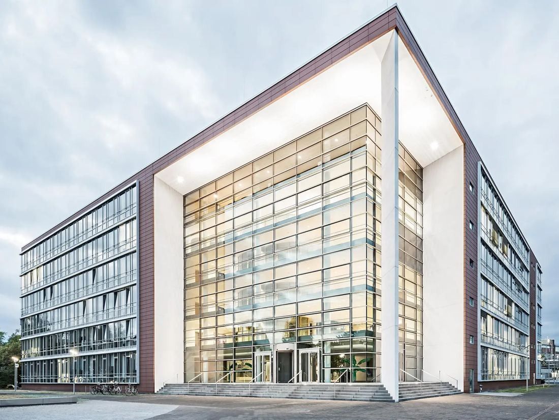 Six-storey office building with a tall glass corner facade framed in white and dark brick