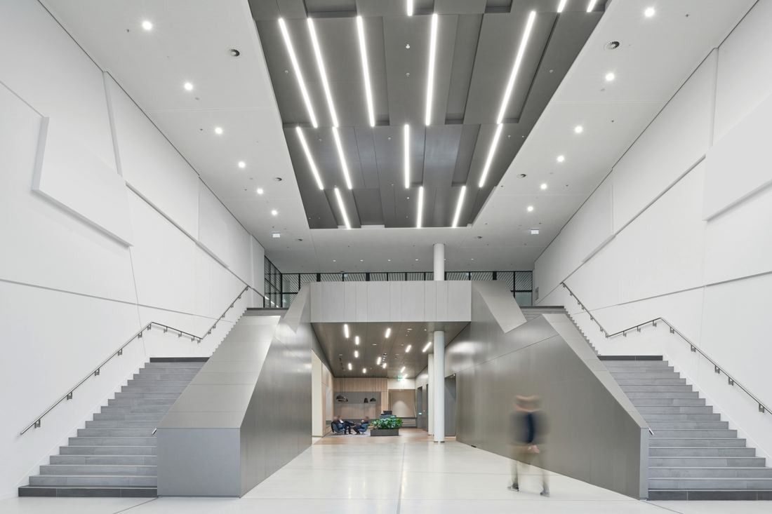 Henkel: Tall white entrance hall with twin stairs and linear ceiling lights