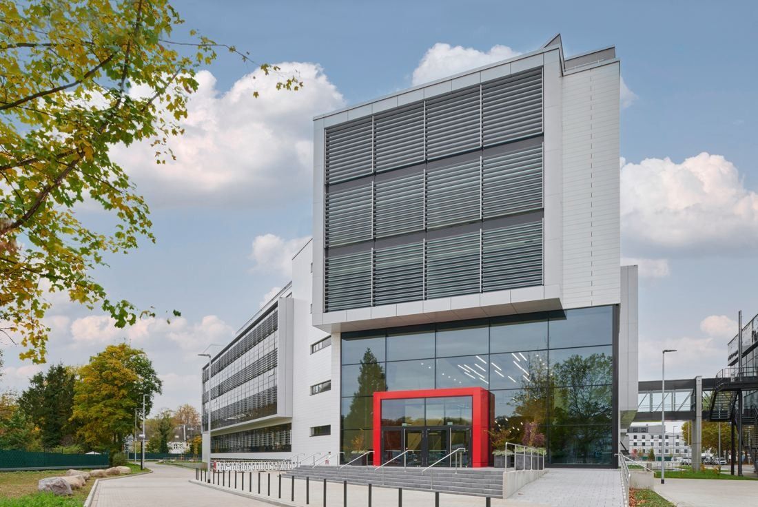 Henkel: White building with louvred upper facade and a red entrance frame among trees