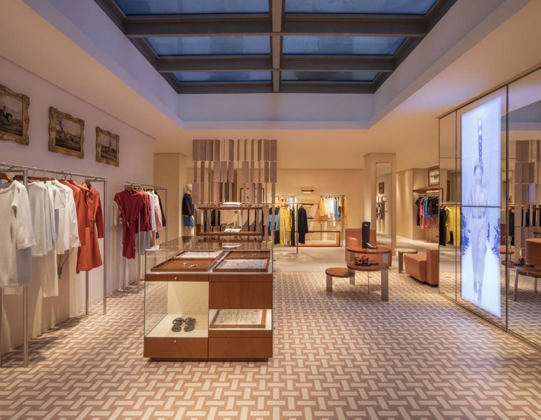 Bright store floor under a large skylight, with clothing rails, display tables and a patterned floor