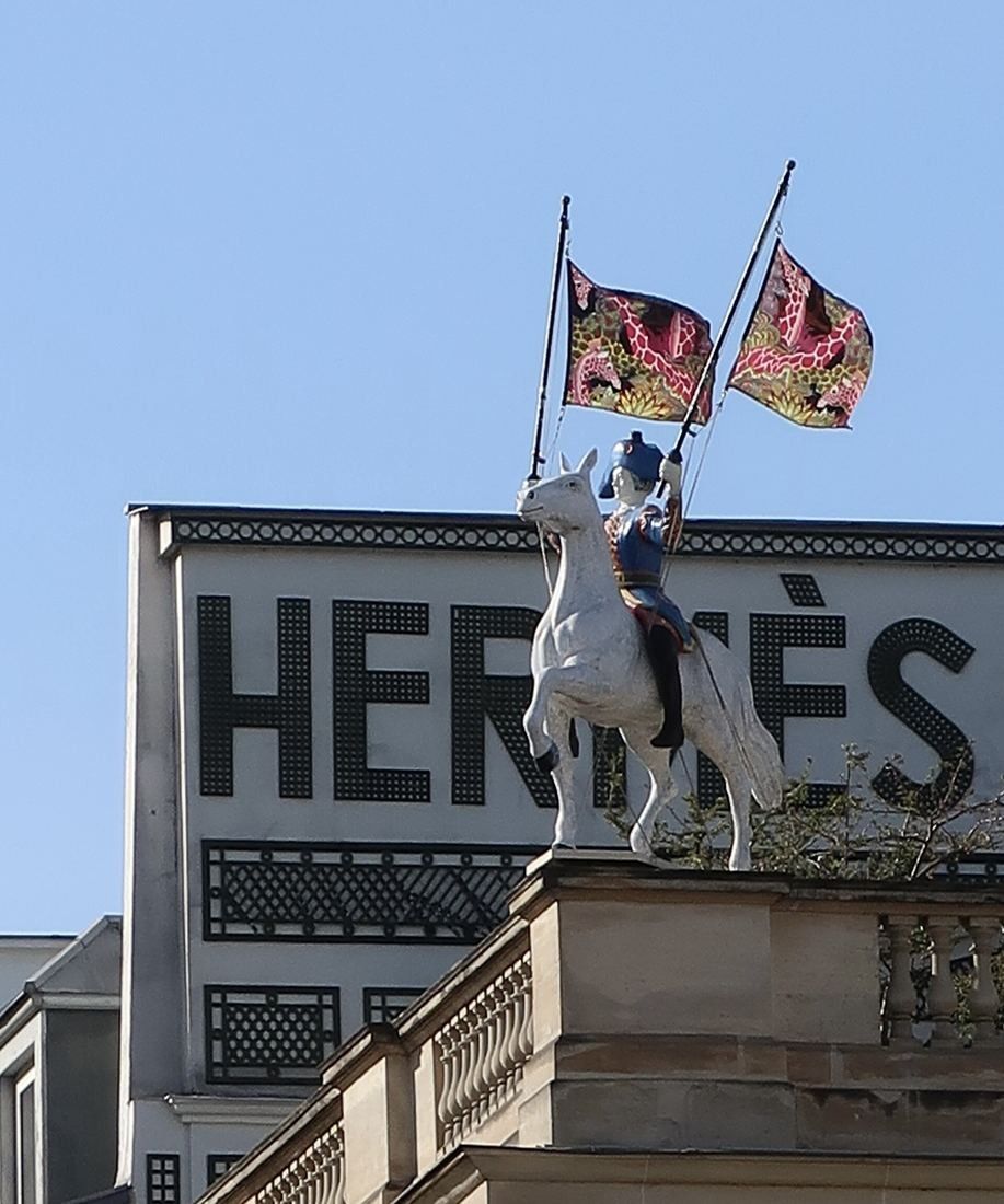 Hermès: Close view of a rider statue holding two flags on a roof balustrade