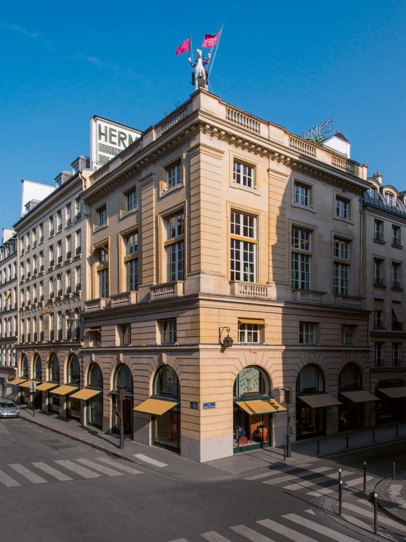 Hermès: Corner stone building with arched ground-floor windows and a rider statue holding flags on the roof