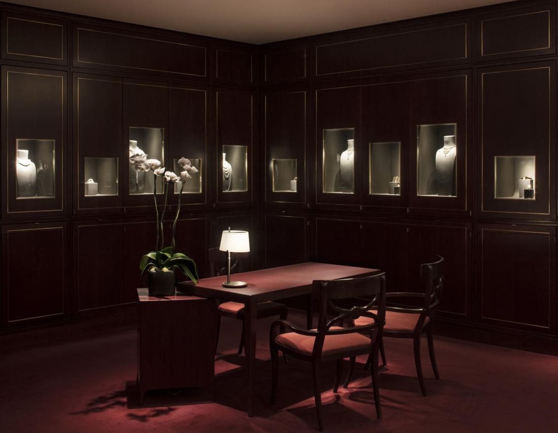 Hermès: Dark panelled room with lit wall niches, a table and red chairs