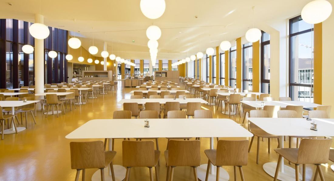 Hermès: Large staff restaurant with white tables, wooden chairs and globe pendant lights