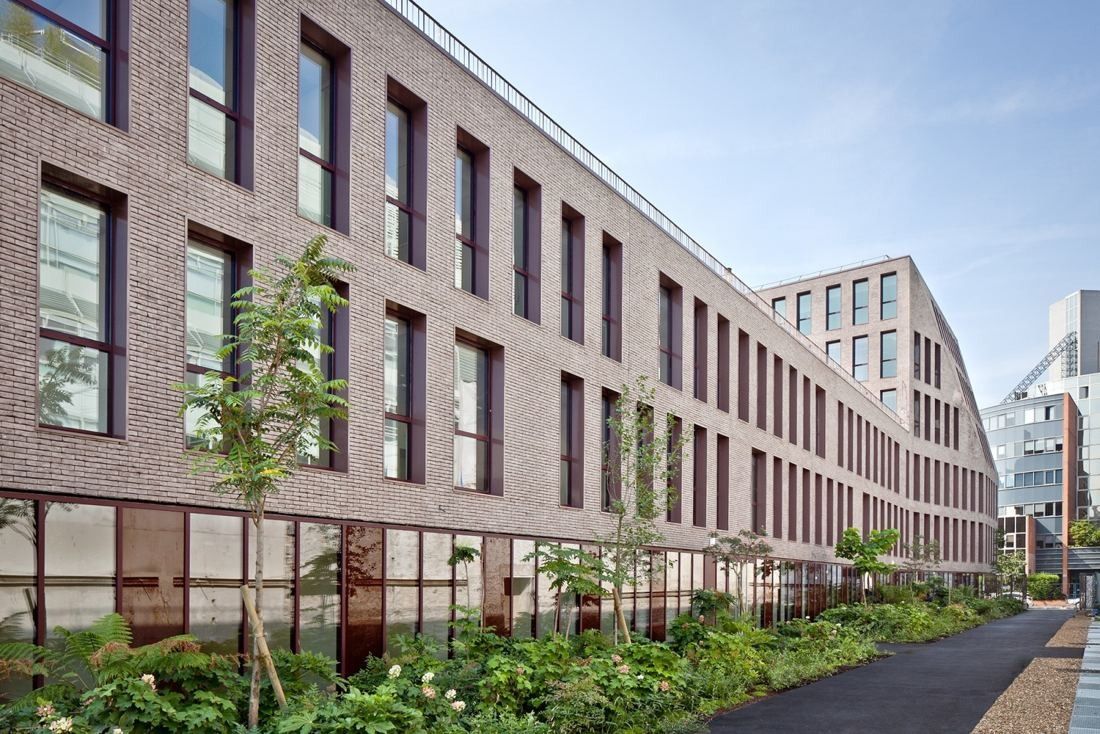 Hermès: Long brick building along a street lined with young trees and plantings