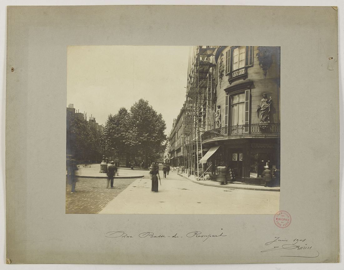 Old black-and-white photograph of a tree-lined street with tall buildings and a few pedestrians