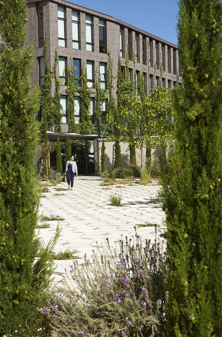 Hermès: Paved garden path between cypress trees leading to a brick building