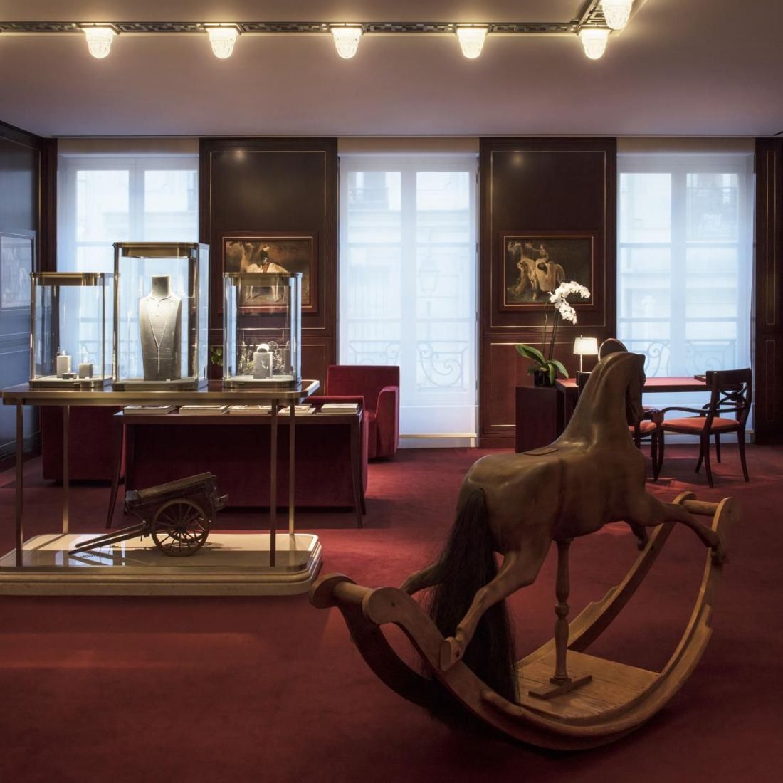 Hermès: Room with red carpet, framed paintings, display cases and a wooden rocking horse