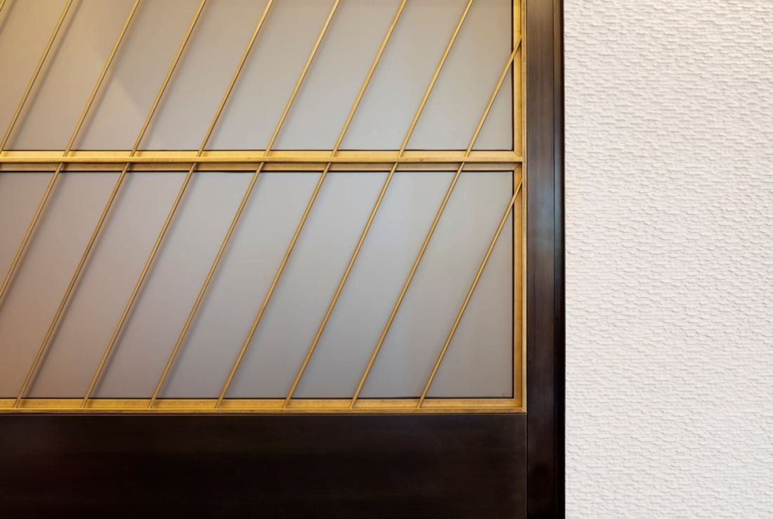 Hilton: Close-up of a screen with diagonal brass lines next to a textured white wall