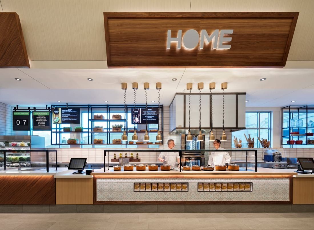 Hilton: Food station under an illuminated HOME sign with open shelving and pendant lights
