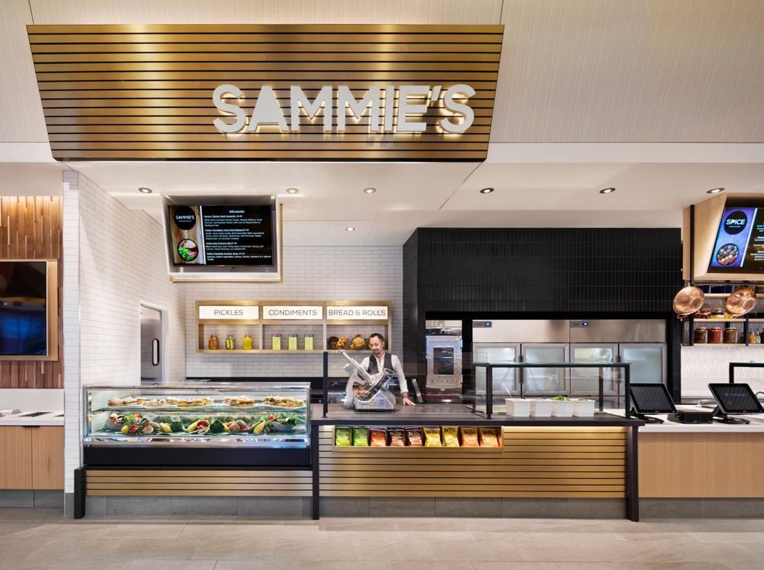 Hilton: Sandwich counter under a slatted SAMMIE'S sign with a refrigerated display