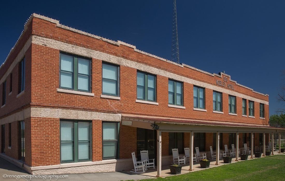 Two-storey red brick hotel with a long covered porch and rocking chairs