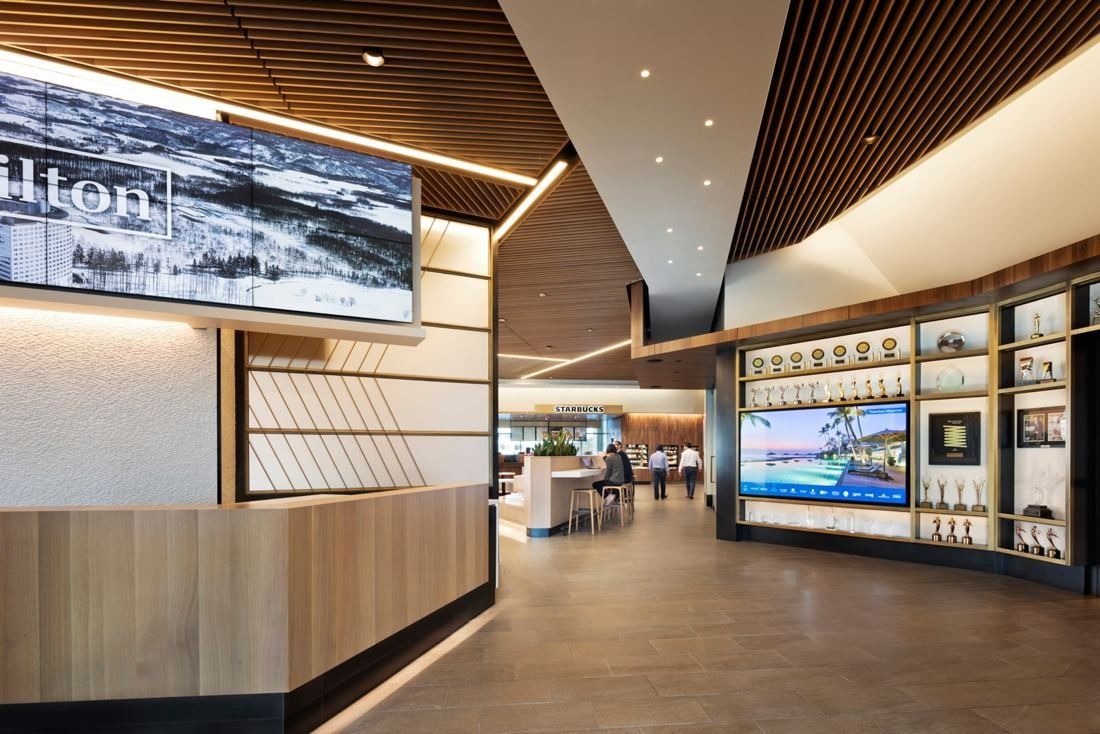 Hilton: Wood counter with a large screen and backlit display shelves under an angled ceiling