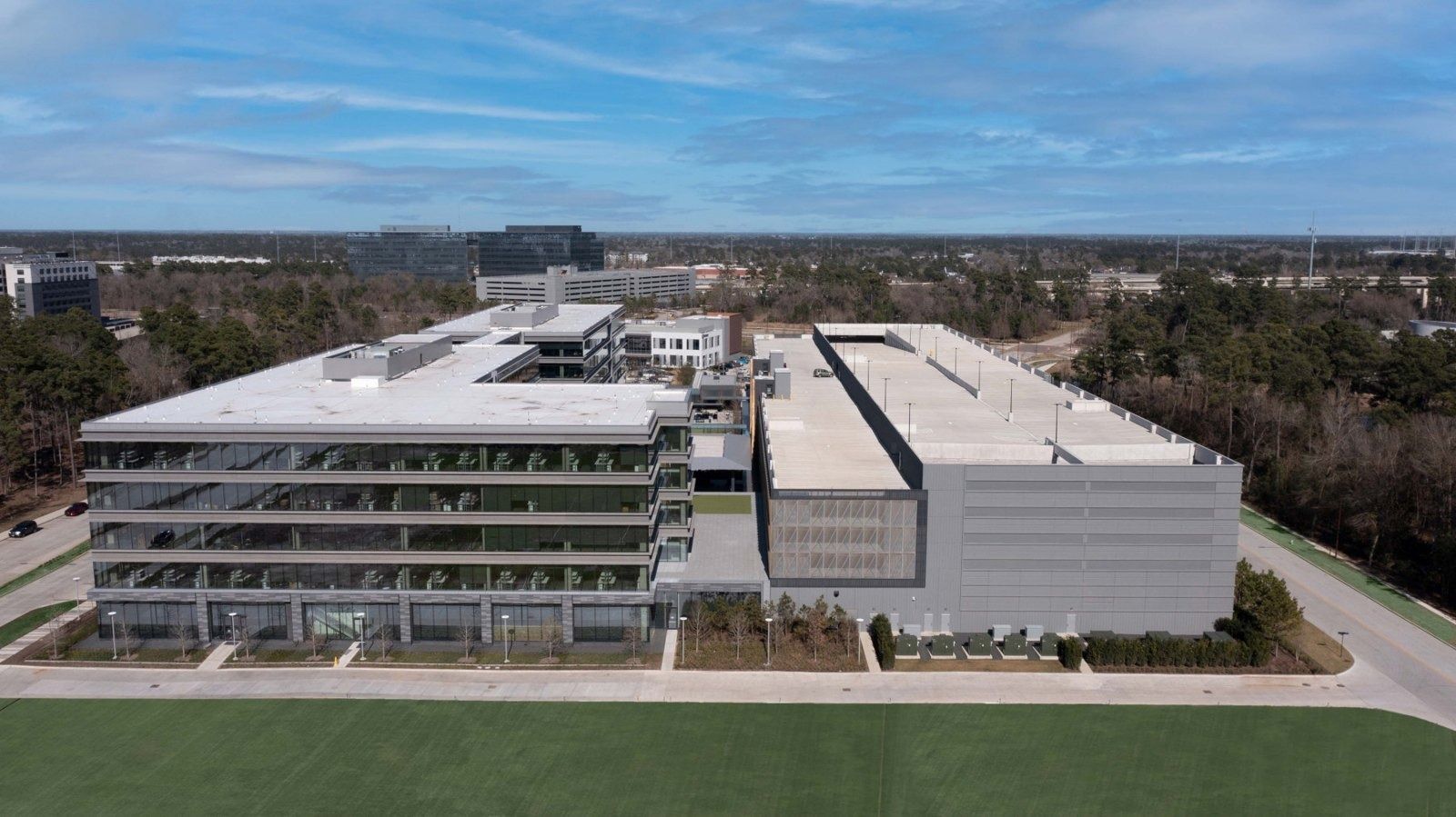 Hewlett Packard Enterprise: Aerial view of a multi-story office building and a large adjacent structure surrounded by woodland