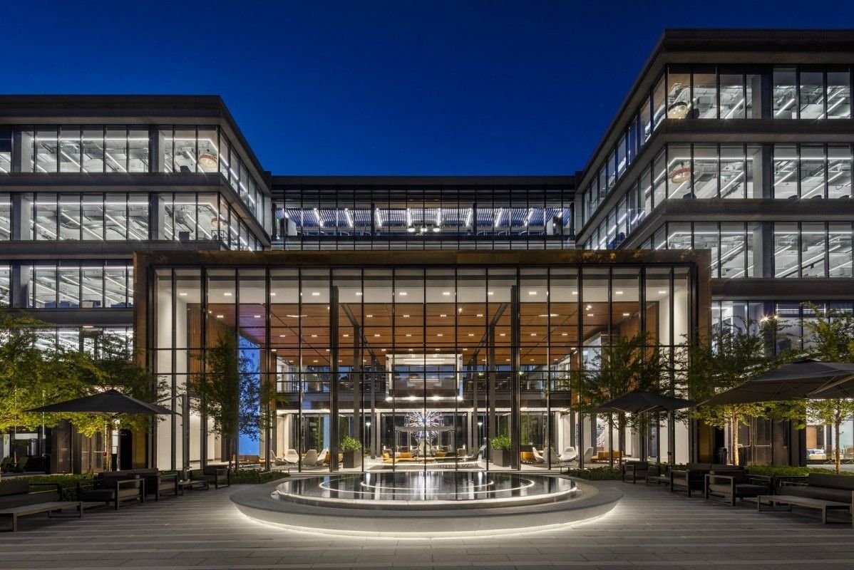 Hewlett Packard Enterprise: Courtyard at twilight with a lit glass entrance hall and a circular pool between two office wings